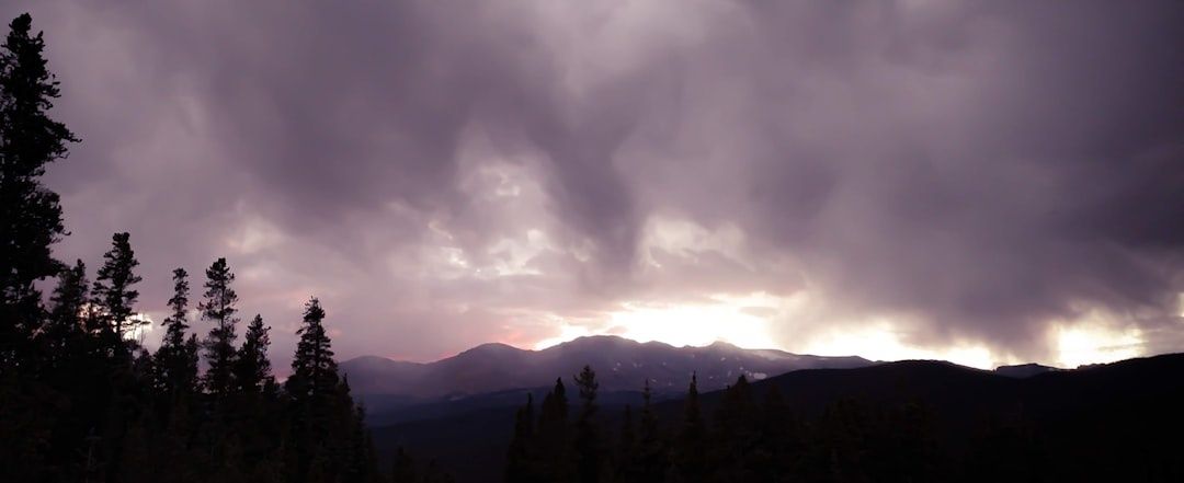 Dark storm clouds gather over Colorado mountains and silhouetted trees