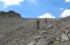 Two hikers descend a steep, loose scree slope beneath a blue sky