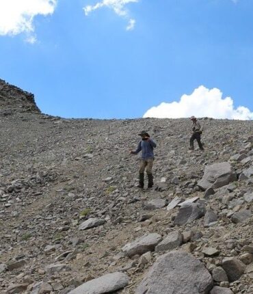Two hikers descend a steep, loose scree slope beneath a blue sky