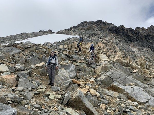 Hikers carefully descending a steep, rocky talus slope below a mountain ridge